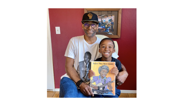 A Black father wearing baseball cap holds a coloring book with his son